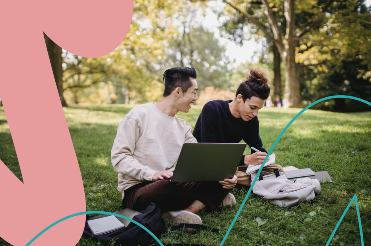Two people sitting on a grassy field working on a laptop