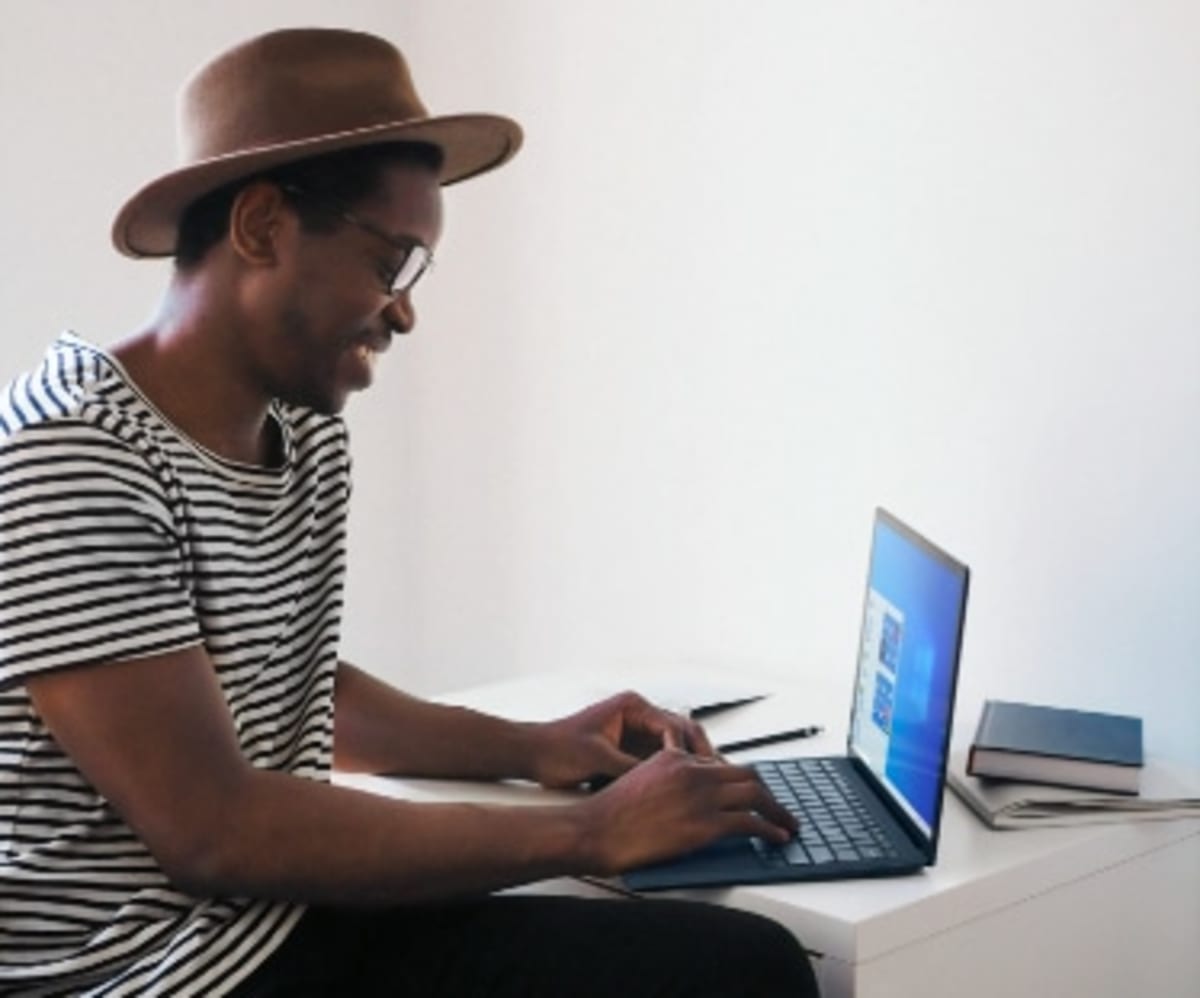 Man wearing a hat typing on his laptop