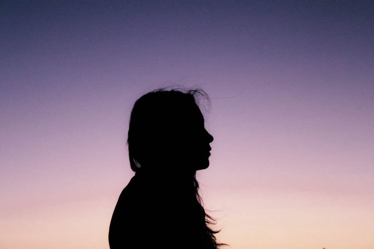 Sillhouette of a woman standing in front of a sunset