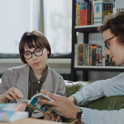 Two people wearing glasses reading in a library. 
