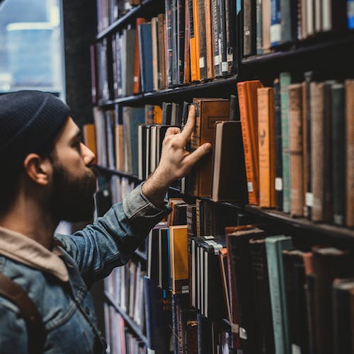 Man in a library reaching for a book, symbolising right skilling