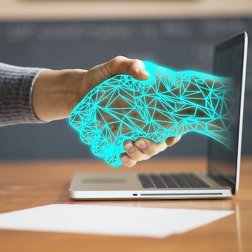 Person shaking hands with a digital arm coming out of a laptop, symbolising unconscious bias in technology