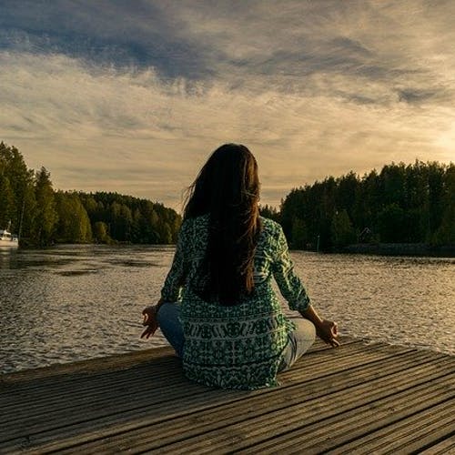 Woman sitting cross legged practicing mindfulness meditation in front of a lake. 