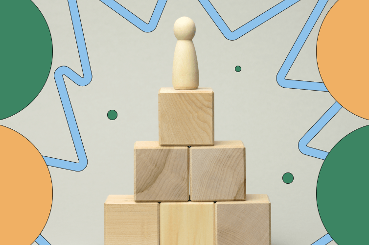 Wooden human figurine on top of a small pyramid of wooden blocks