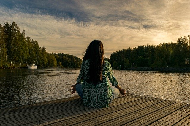 Woman sitting cross legged practicing mindfulness meditation in front of a lake. 